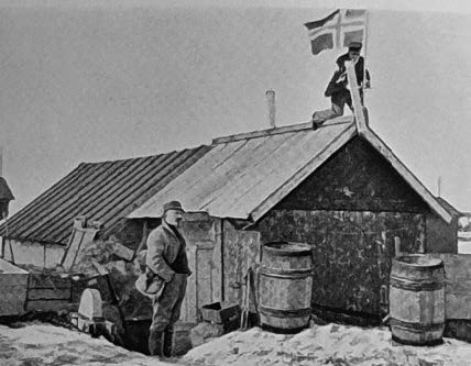 Messeforstander Zapffe foran spisebrakken «Speilen» på Kings Bay i 1925. På taket heiser seilmaker Rønne det norske flagget. Bilde fra Zapffes bok om Roald Amundsen (1935).